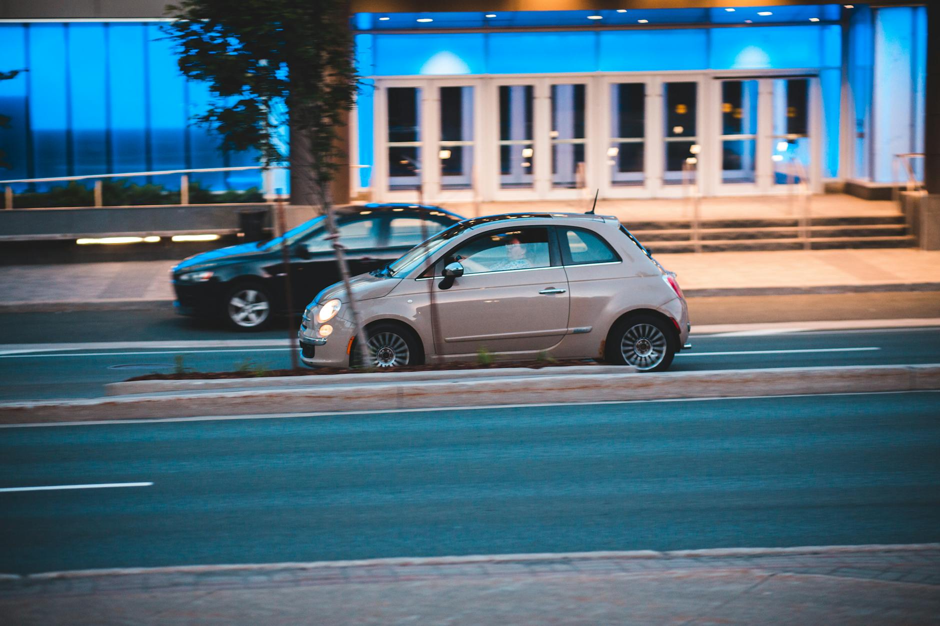 Fiat 500 jedzie nocą obok nowoczesnego, niebiesko oświetlonego biurowca